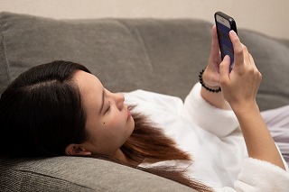 寝そべってスマートフォンを触る女性